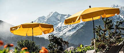 Entspannung pur auf Sonnenliegen unter gelben Sonnenschirmen vor einer spektakulären Alpenkulisse