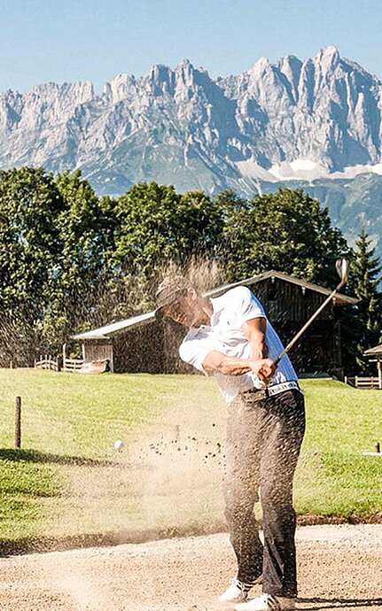 Golfer schlägt Ball aus Sandbunker vor alpiner Kulisse im Salzburger Land