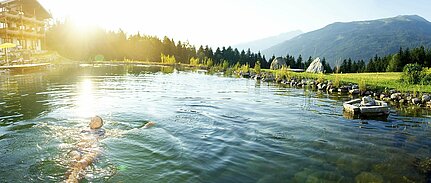 Frau genießt das Schwimmen im natürlichen Schwimmbiotop des Wellnesshotels Sonnberghof im Nationalpark Hohe Tauern