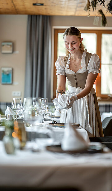 Freundliche Bedienung im traditionellen Dirndl deckt den Tisch im Restaurant des Sonnberghofs
