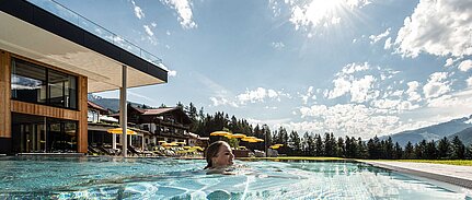 Frau genießt die Sonne im Panoramapool des Wellnesshotels mit Blick auf die Alpen