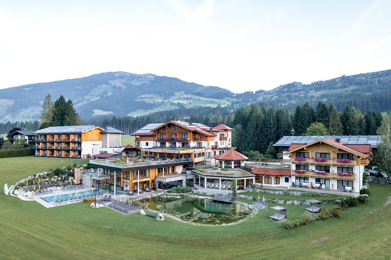 Panoramablick auf das Naturhotel Sonnberghof mit Außenpool und Badeteich im Salzburger Land.