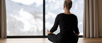 Frau in Meditationshaltung vor einer beeindruckenden Bergkulisse im Sonnberghof